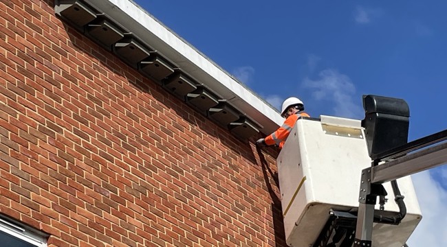 National Grid engineer in cherry picker installs swift boxes at Honiton Primary School