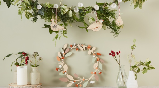 Christmas garland with wooden birds below are white vases containing flowers and a wooden garland in the centre