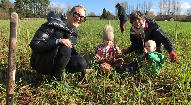 two figures and two children alongside newly planted trees