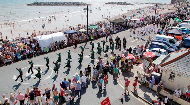 Aerial view of SIdmouth seafront with sea in the distance and crowd watching a procession