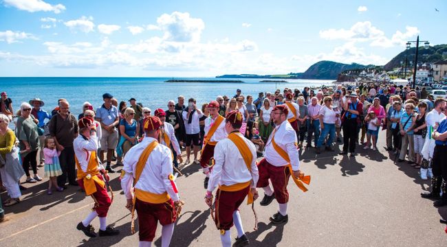 Morris Dancers watched by crowd with the sea in background