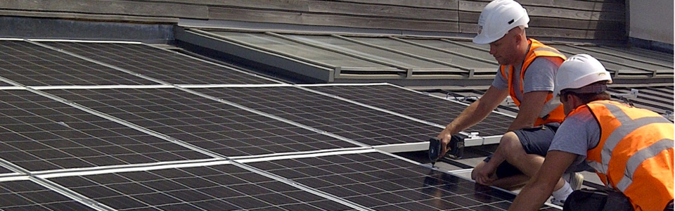 Two workmen installing solar panels on a roof with the EDDC and Funded by UK Government Logos 