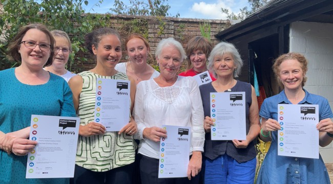 a group of eight women holding up certificates in a walled garden 