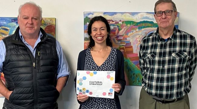 Councillor Paul Arnott with EDDC’s new cultural producer Sarah Elghady and Cllr Nick Hookway. The paintings in the background are by artist Michael Buckland. Credit: EDDC).