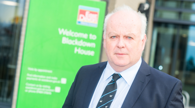 Photo of Councillor Arnott in front of the entrance to Blackdown House