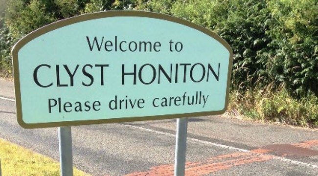 Photo of a sign post 'welcome to Clyst Honiton. Please drive carefully'