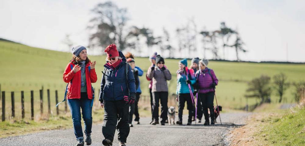 A group of people walking along a path whilst talking, with trees in the background