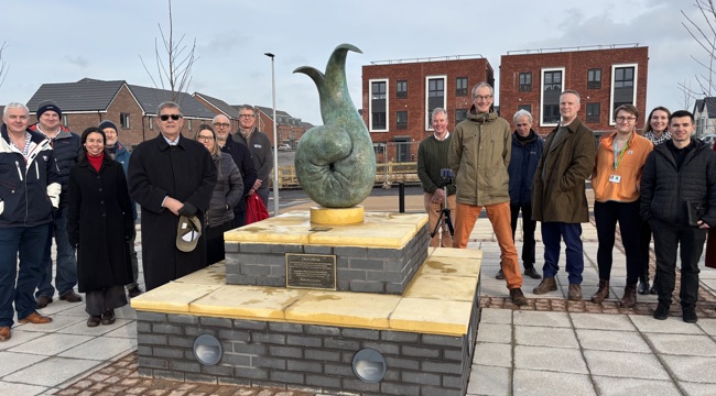 Group of people outside surround aged bronze sculpture on a plinth 