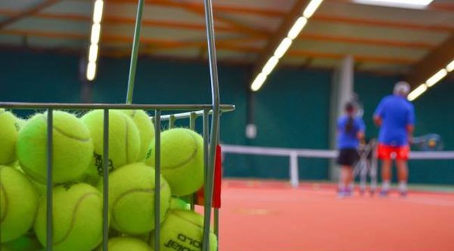Photo from Exmouth Tennis and Fitness Centre of tennis balls in the foreground and in the background a court with tennis players 