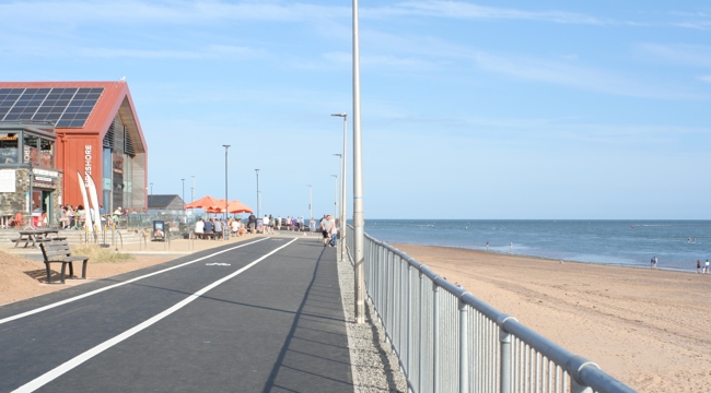 The resurfaced path in front of Sideshore, with the beach to the right and blue sky above