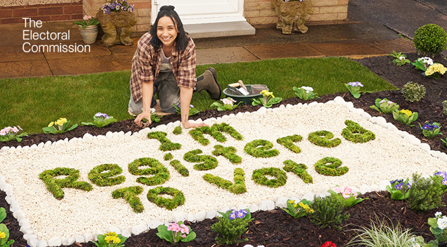 Photo of a person next to a flower bed arranged to spell 'I'm registered to vote'